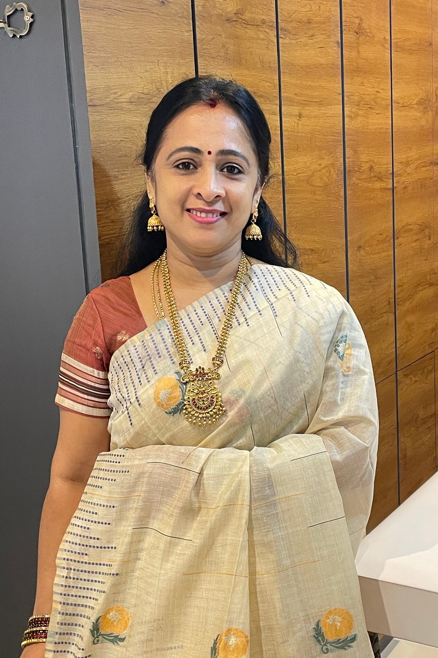 Woman in a traditional outfit with embroidery, standing indoors on a wooden floor.